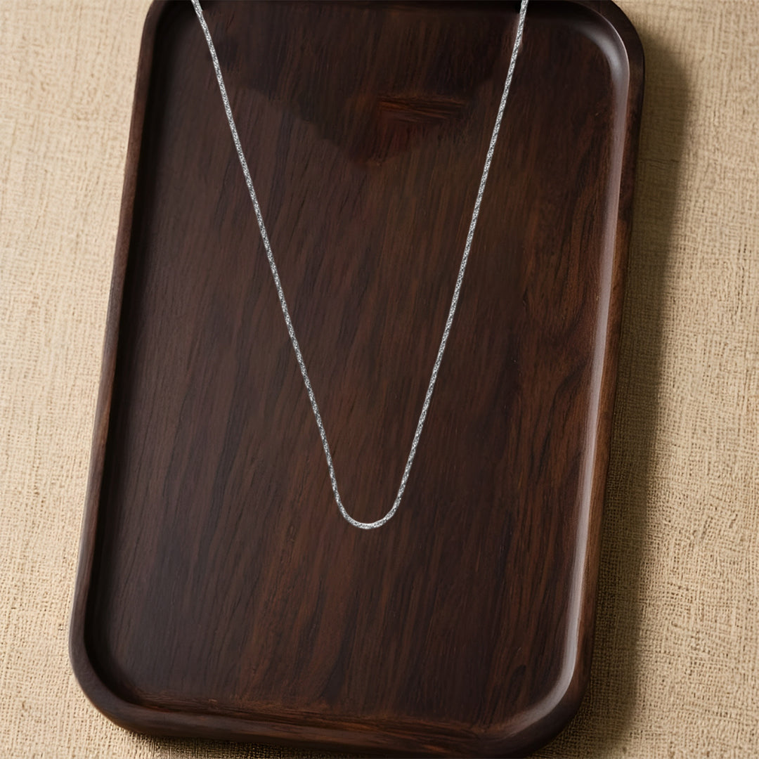 silver necklace on a dark wooden tray with a beige fabric background